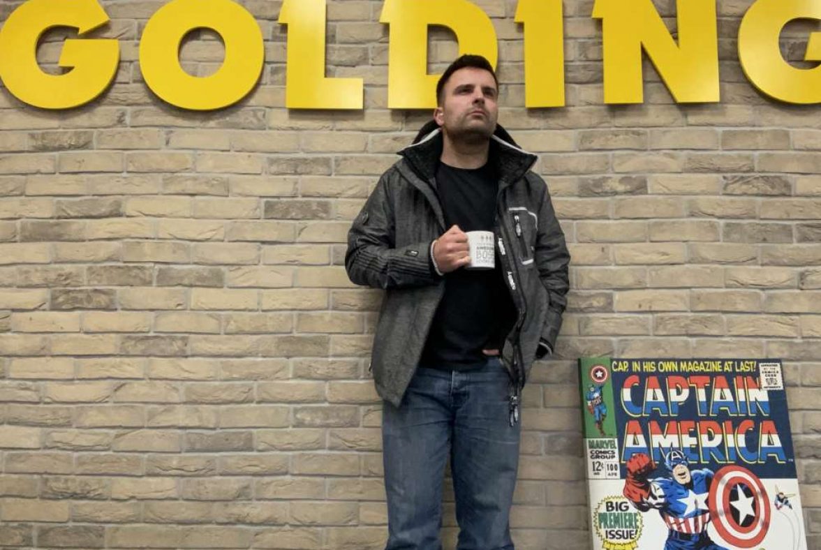 Ian Butler standing against a wall with their logo behind